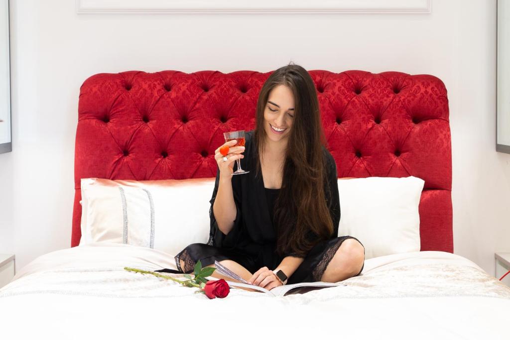 a woman sitting on a bed holding a glass at Adrian D'Cap Boutique Manor in Stellenbosch