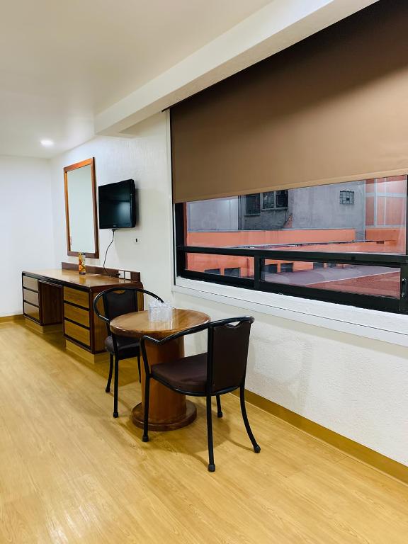 A bright guest room with a small table, two chairs, a desk and a street-facing window.