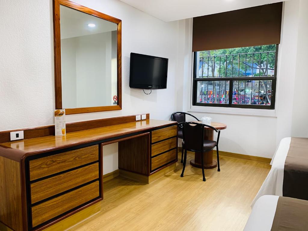 A compact guest room with a long desk, mirror and window.