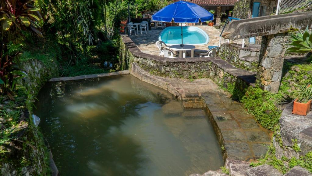 uma piscina de água com uma mesa e um guarda-sol em Pousada do Escultor em Cachoeiras de Macacu