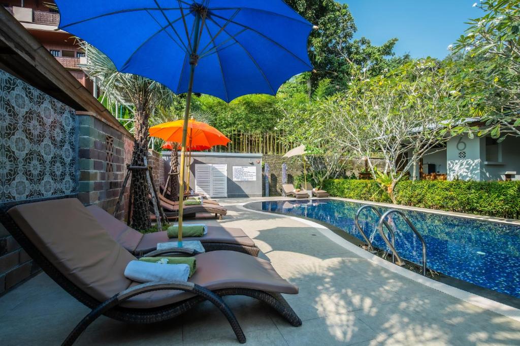 eine Gruppe von Stühlen mit einem Sonnenschirm neben einem Pool in der Unterkunft Kata Tranquil Villa - SHA Plus in Karon Beach