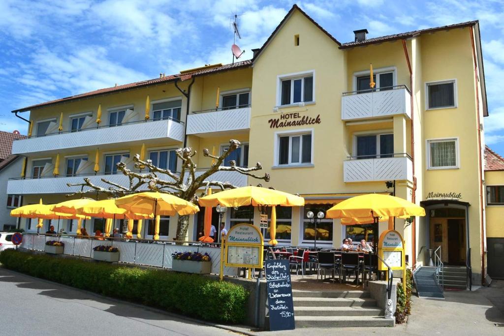 un hôtel avec des tables et des parasols devant lui dans l'établissement Hotel & Restaurant Mainaublick, à Uhldingen-Mühlhofen