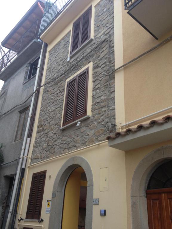 - un bâtiment avec un mur en pierre et des fenêtres dans l'établissement Basicò un balcone sul mare - Casa SALITA FOTI -Case vacanza Sicilia&Toscana-, à Basicò