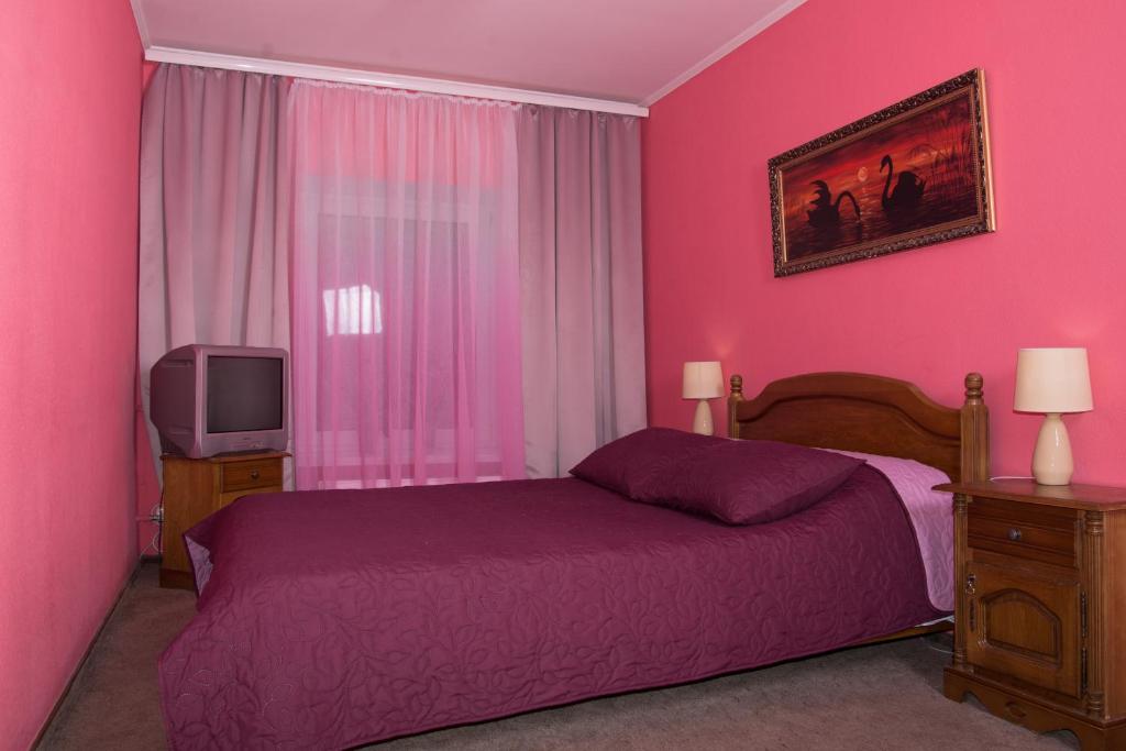 Habitación de color rosa con cama y TV en Knaus Apartments, en Chernivtsi