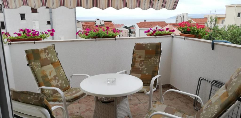 - une table et des chaises blanches sur un balcon fleuri dans l'établissement Apartman "TRI MASLINE", à Makarska