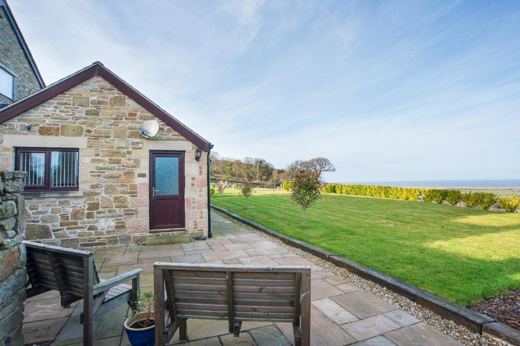 a stone house with two benches in front of a yard at Finest Retreats - Sea Views Cottage in Prestatyn