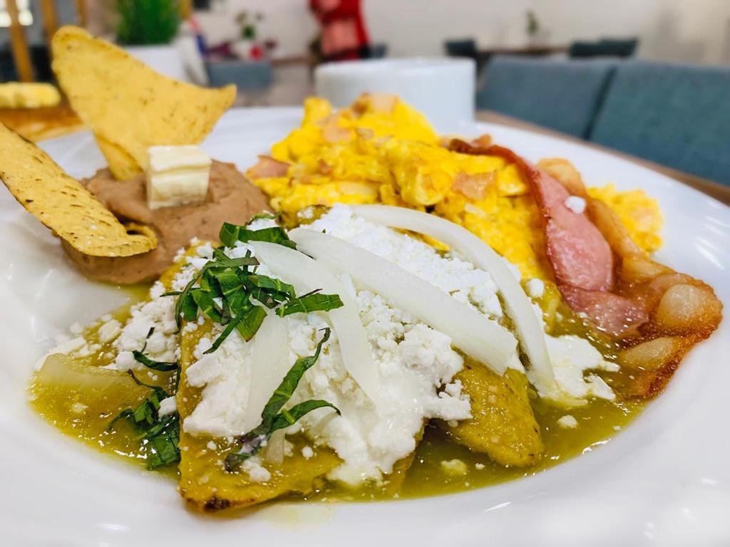 A cooked breakfast plate with enchiladas, eggs and bacon.