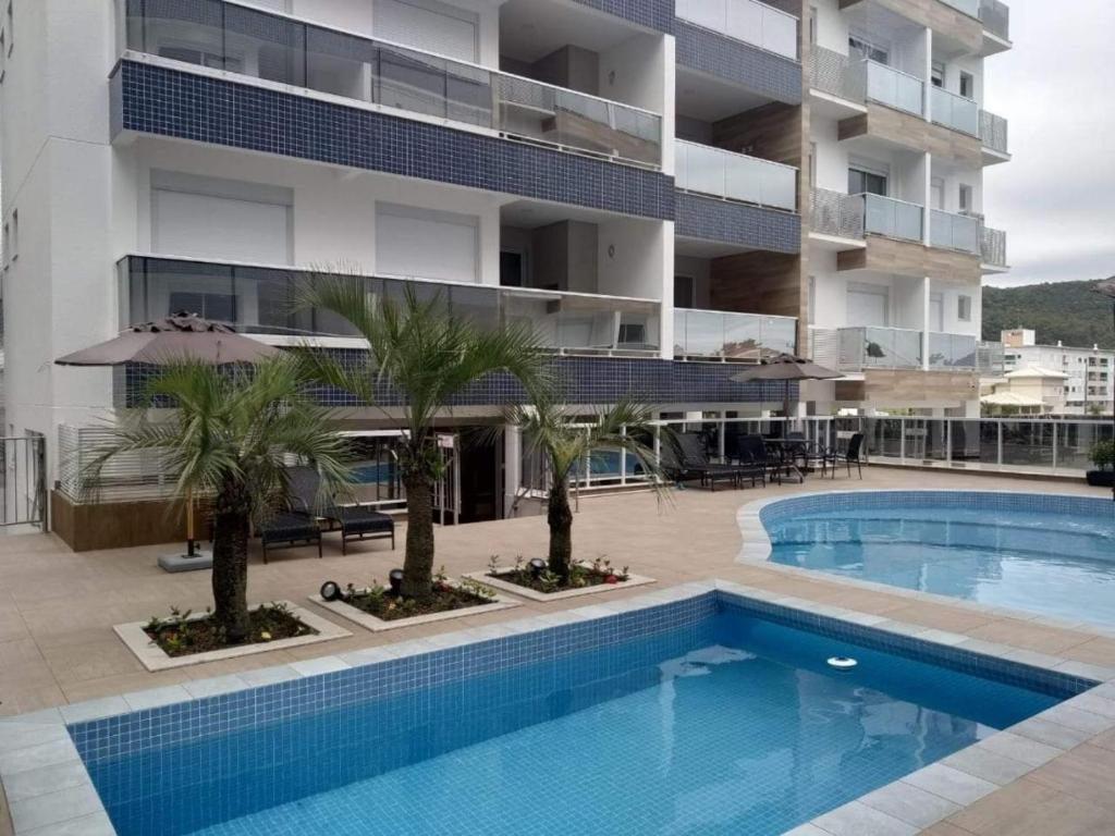 una piscina con palmeras frente a un edificio en Duplex lindo sofisticado, en Governador Celso Ramos