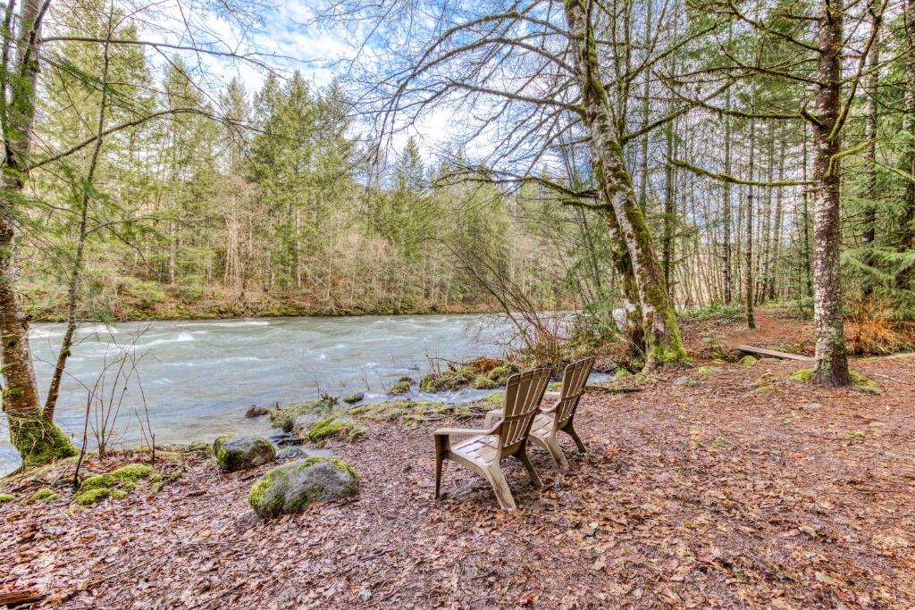 duas cadeiras sentadas em frente a um rio em Zoe's Log Cabin em Welches