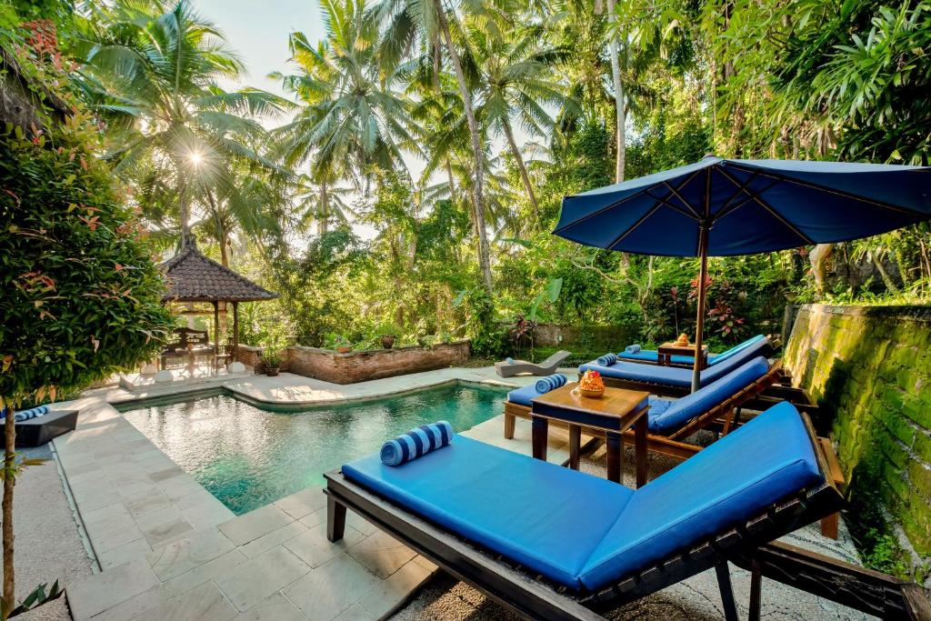 a pool with two blue lounge chairs and an umbrella at Kebun Indah Ubud in Ubud