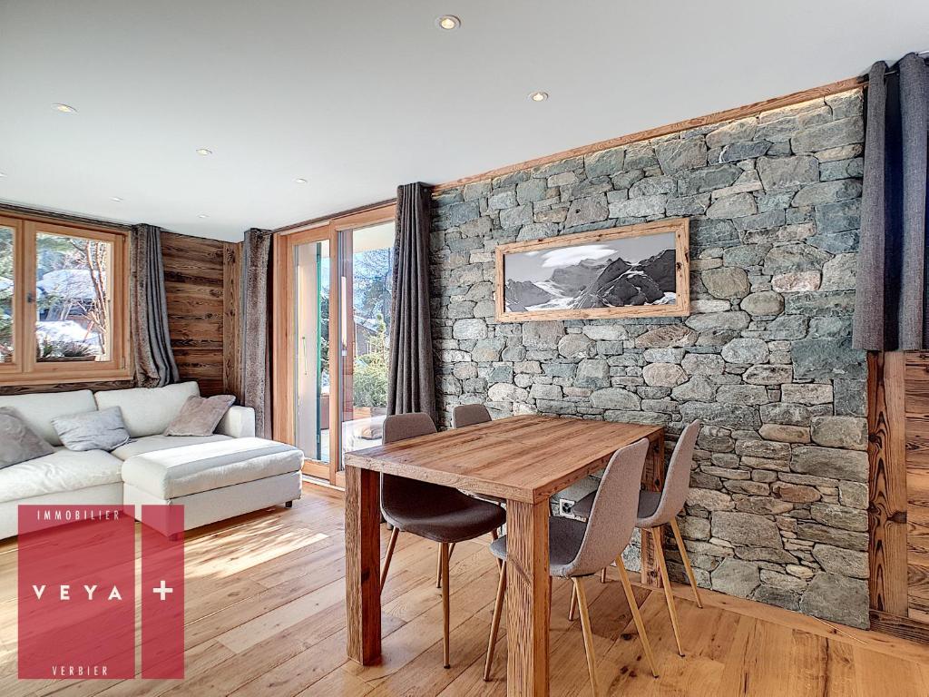 sala de estar con mesa de madera y pared de piedra en Erika 012 en Verbier