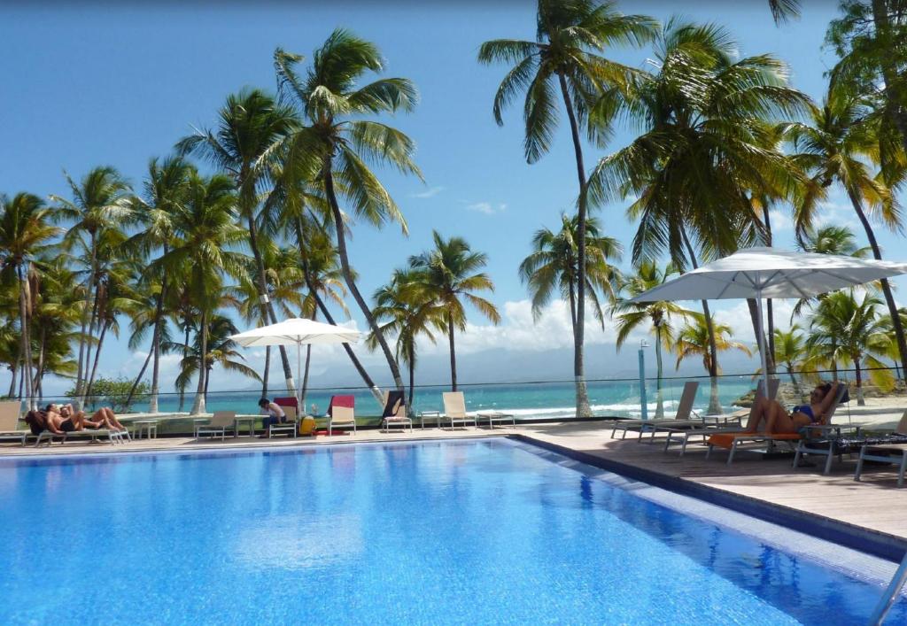 una piscina con palmeras y el océano en Hotel Fleur d'Epee, en Le Gosier