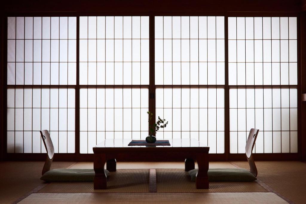 a room with a table and two chairs in front of a large window at Tsukasaya Ryokan in Tsuruoka