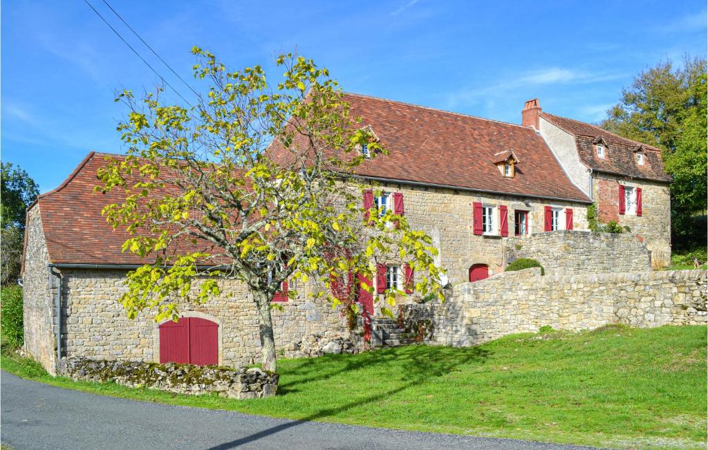 stary kamienny dom z czerwonymi drzwiami i drzewem w obiekcie Cozy Home In Mayrinhac-lentour With Private Swimming Pool, Can Be Inside Or Outside w mieście Mayrinhac-Lentour