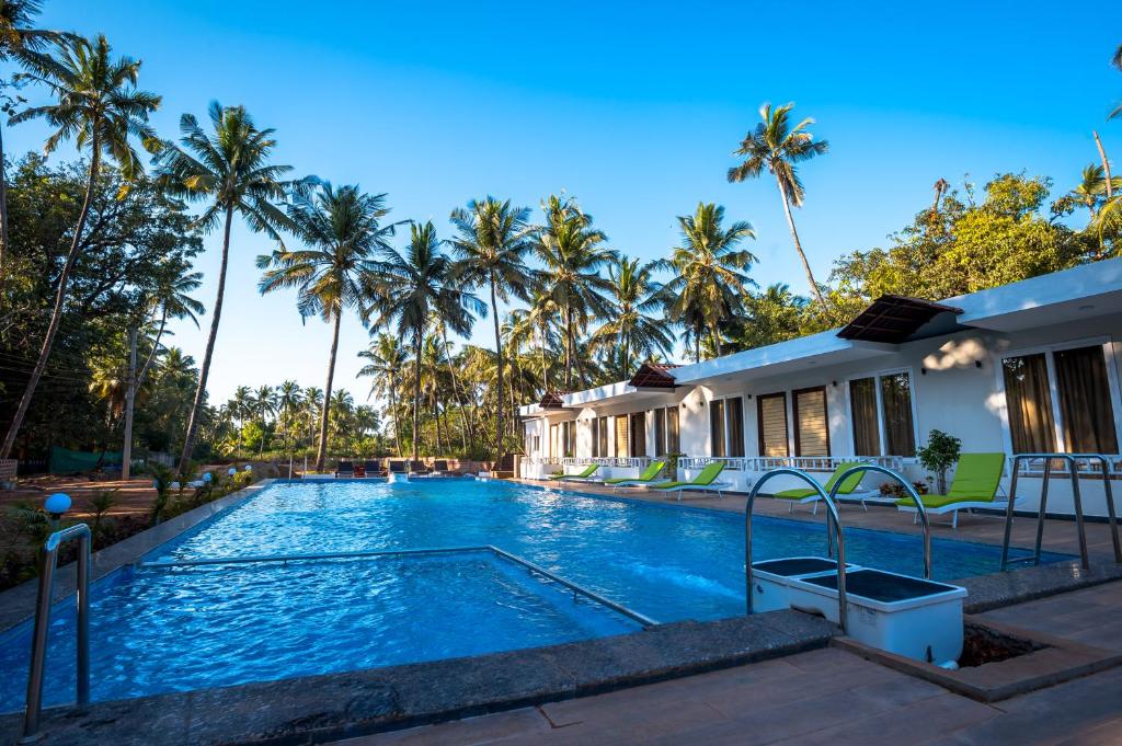 a swimming pool in front of a house with palm trees at Golden Sands Resort, Morjim in Morjim