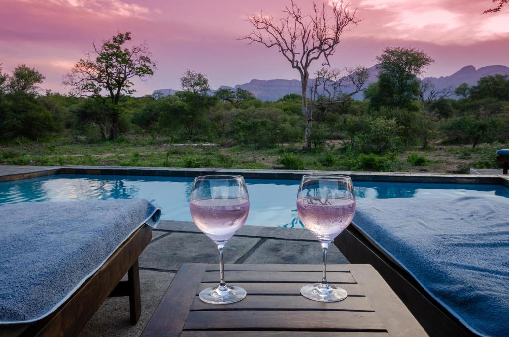 two wine glasses sitting on a table next to a swimming pool at Hidden 2-Bedroom Gem In A Quiet Wildlife Estate in Hoedspruit
