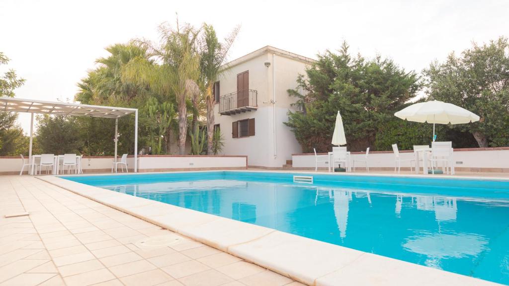 een zwembad met een parasol en een gebouw bij Villa Calò in Castelvetrano Selinunte