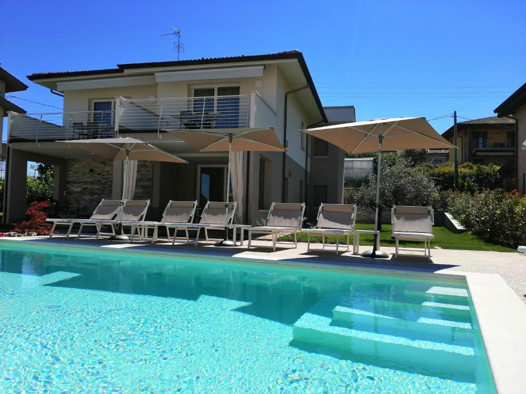 a swimming pool with chairs and umbrellas in front of a house at COSTA DEL GARDA - Lazise in Lazise