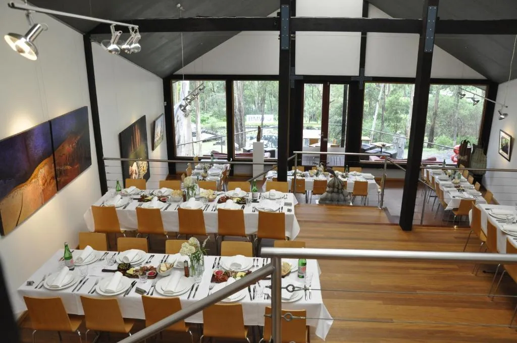 A dining room with set tables, timber beams and windows onto the trees
