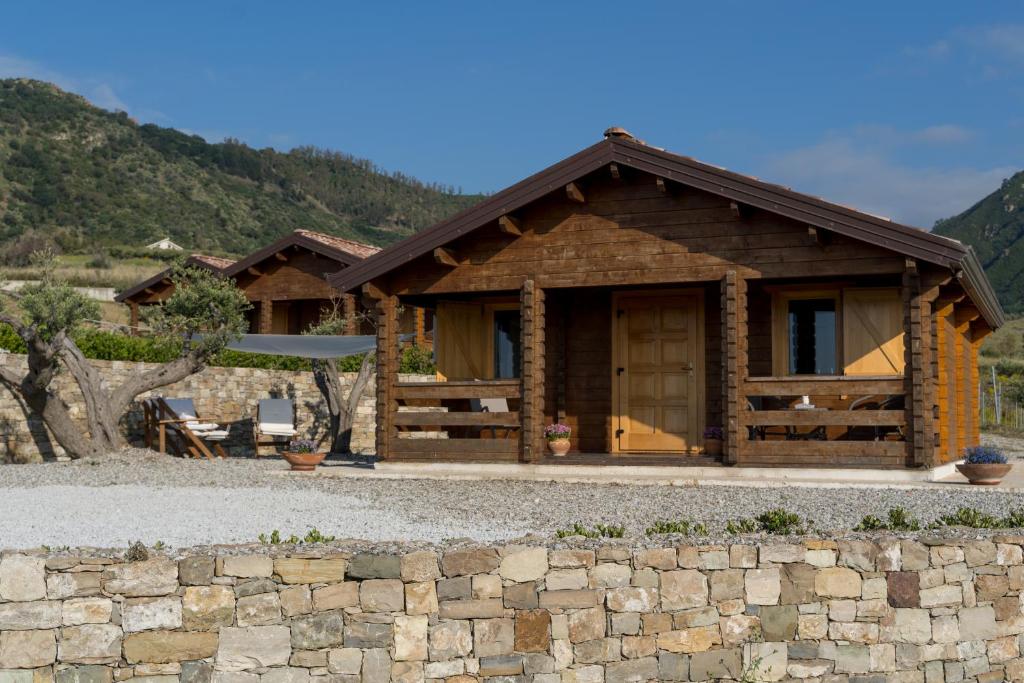a log house with a stone wall in front of it at Chalet Tenuta Lacco in Furnari