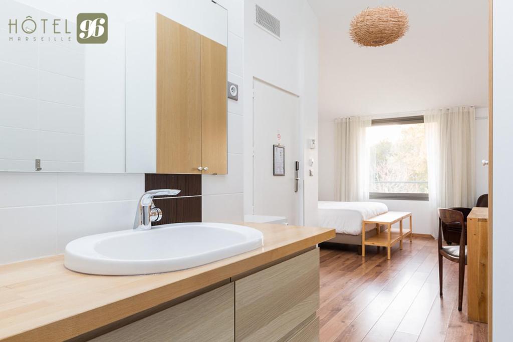 a white bathroom with a sink and a bedroom at Hôtel 96 in Marseille