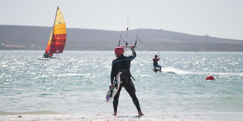 un hombre está de pie en la playa con un velero en Kite Basecamp Langebaan en Langebaan