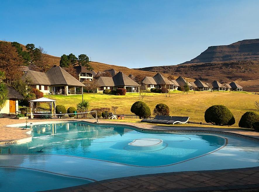 une grande piscine en face d'un tas de cabanes dans l'établissement Fairways Drakensberg Resort, à Drakensberg Garden