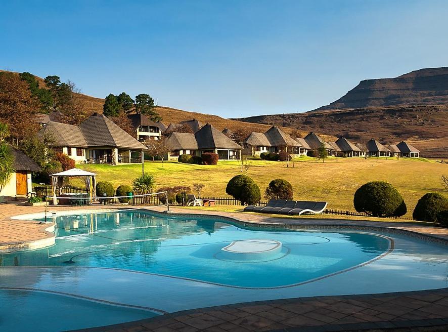 a large swimming pool in front of a bunch of huts at Fairways Drakensberg Resort in Drakensberg Garden