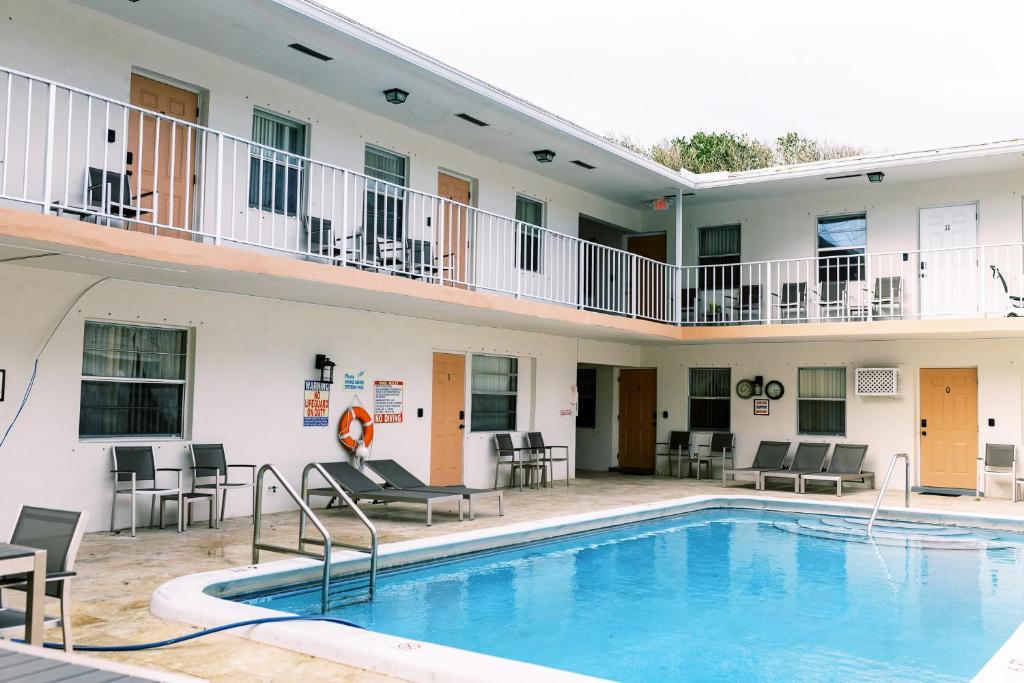 uma piscina em frente a um hotel com cadeiras e mesas em Beachside Gardens Apartments By Lowkl em Deerfield Beach