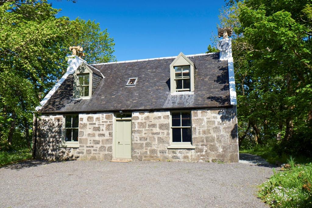 a stone house with a white door on a driveway at Dunvegan Castle Gardens Cottage in Dunvegan