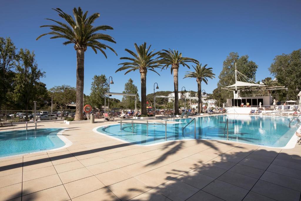 a pool at a resort with palm trees at Minura Cala Galdana & Apartamentos d'Aljandar in Cala Galdana