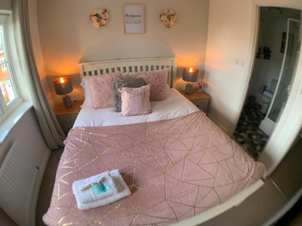 ein kleines Schlafzimmer mit einem großen Bett mit rosa Bettwäsche und Kissen in der Unterkunft Harpers brook house, Netflix TVs and fast WIFI in Corby