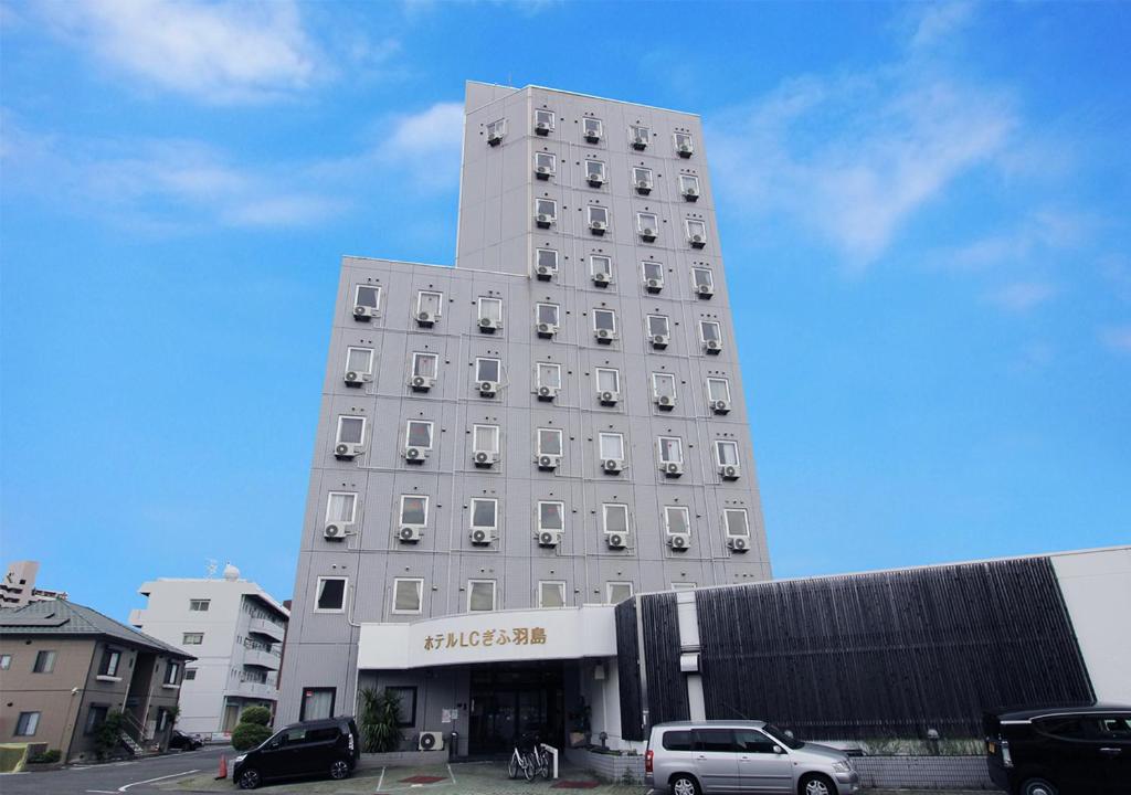 un edificio blanco alto con coches estacionados frente a él en Hotel LC Gifu Hashima en Hashima