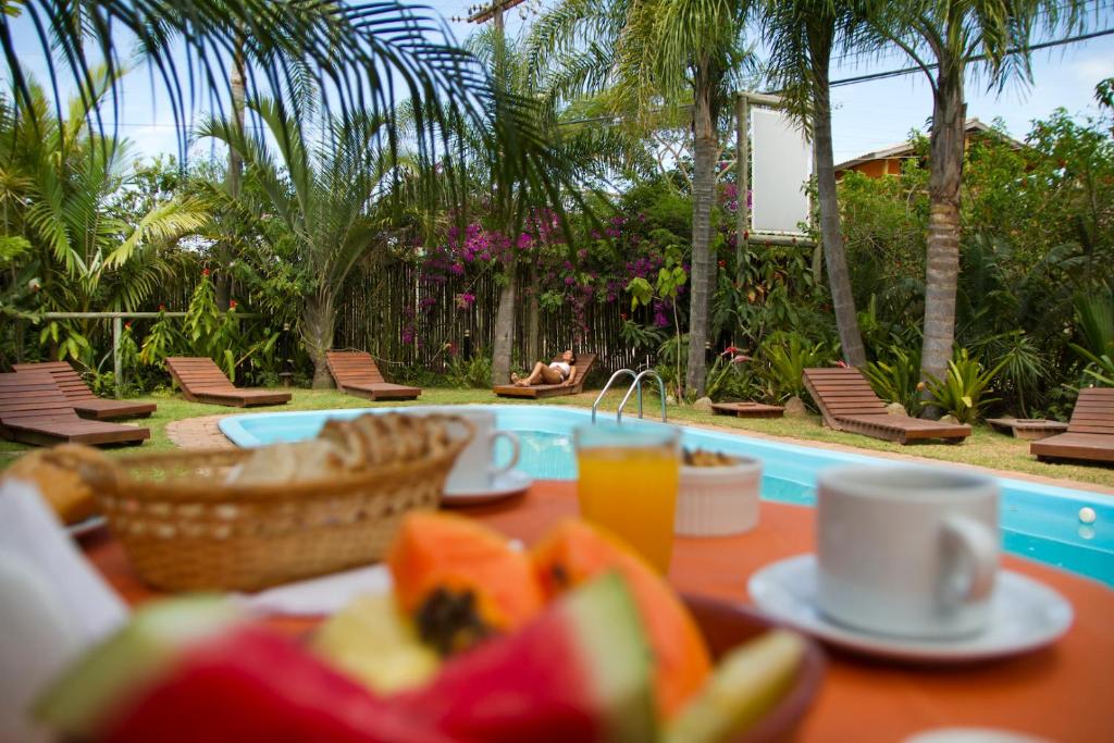 a table with a basket of fruit next to a pool at Pousada Além do Jardim in Praia do Rosa