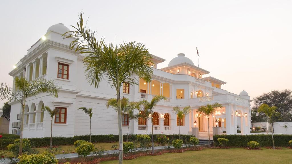 a large white building with palm trees in front of it at Umaid Farm Resort- A Legancy Vintage Stay In Jaipur in Jaipur