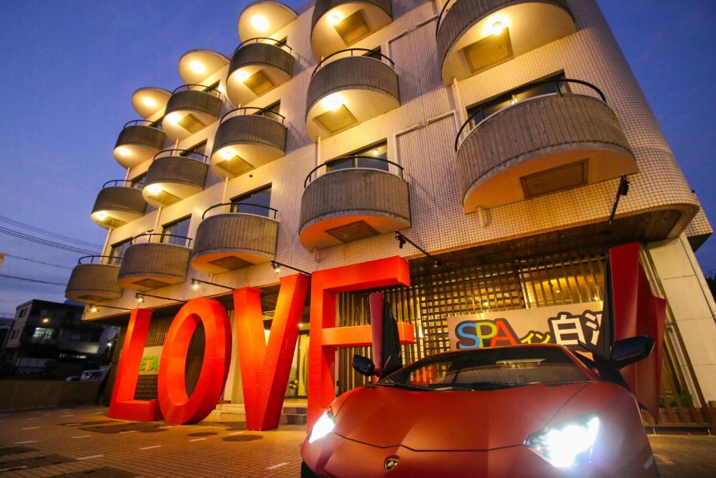 een rode auto geparkeerd voor een gebouw met een liefdesbord bij SPA Inn Shirahama in Shirahama