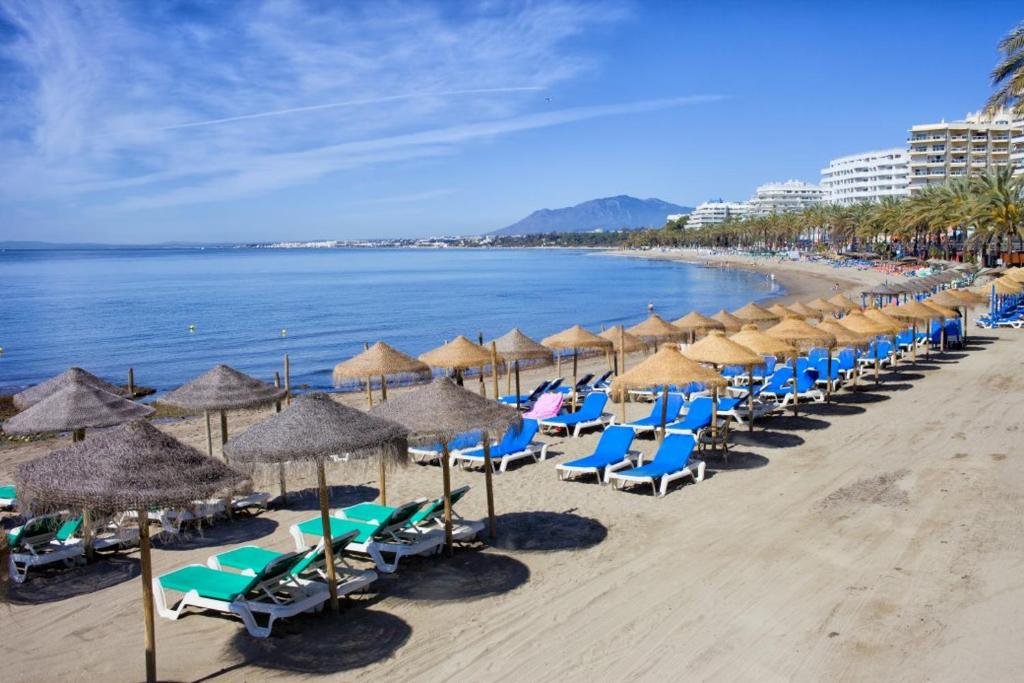einen Strand mit Liegestühlen und Sonnenschirmen und dem Meer in der Unterkunft Playa Fontanilla Apartments in Marbella