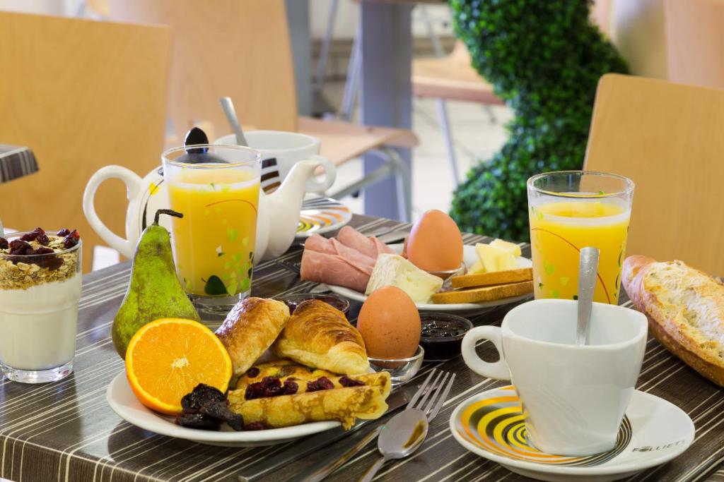 a table topped with plates of breakfast foods and orange juice at The Originals City, Hôtel L&#39;Acropole, Saint-Etienne Sud (Inter-Hotel) in La Ricamarie