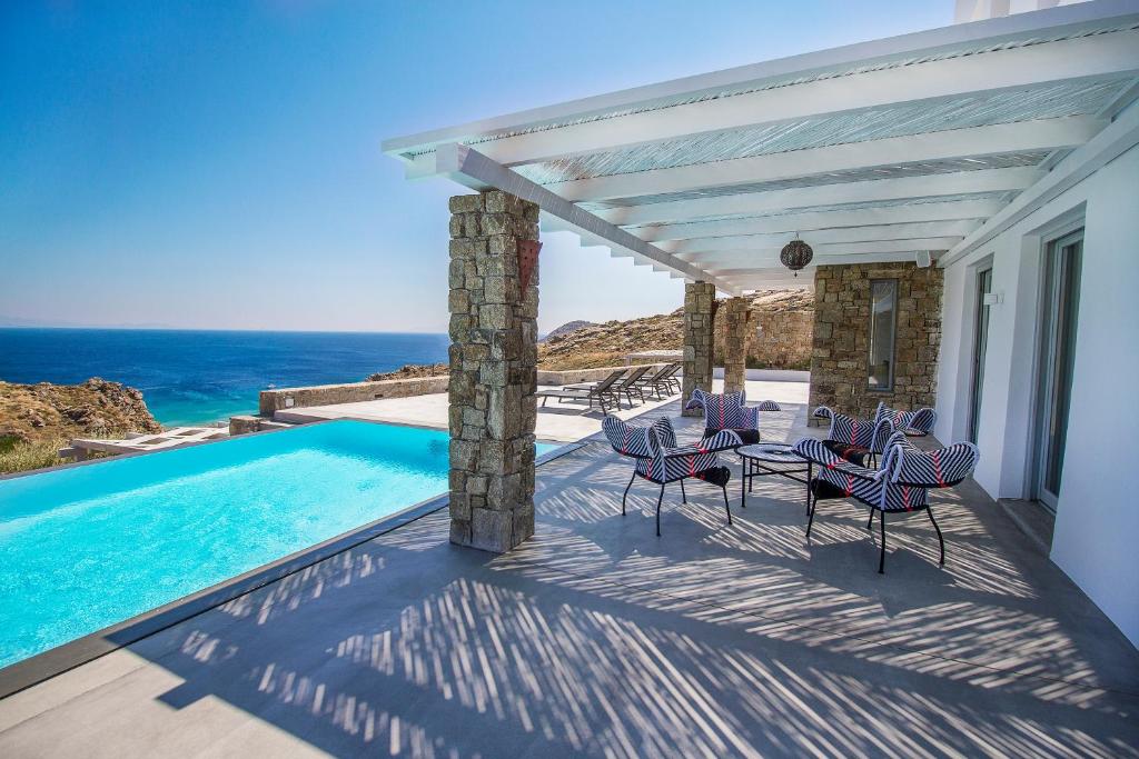 a patio with a pool and chairs and the ocean at Luxury Villa Artemis by Mykonos Luxury in Elia Beach