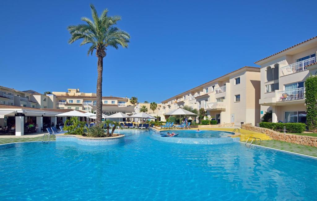 een groot zwembad met een palmboom en gebouwen bij Aparthotel Isla de Cabrera in Colonia Sant Jordi