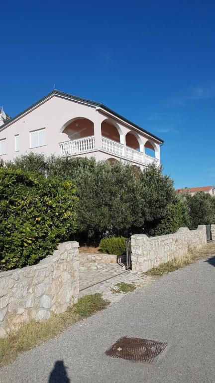 a large white house with a stone retaining wall at Apartments Pink house in Povljana