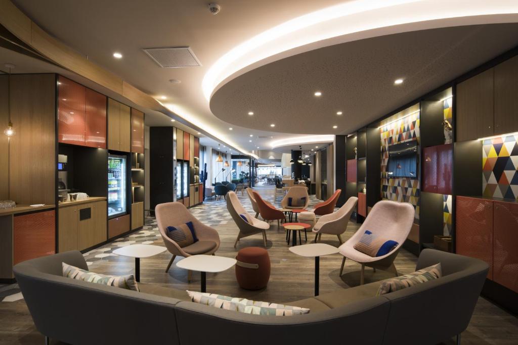 a lobby with chairs and tables in a building at Holiday Inn Express - Paris - CDG Airport by IHG in Roissy-en-France