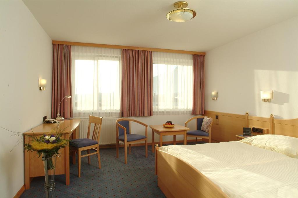 a hotel room with a bed and a table and chairs at Airporthotel Salzburg - Hotel am Salzburg Airport in Salzburg