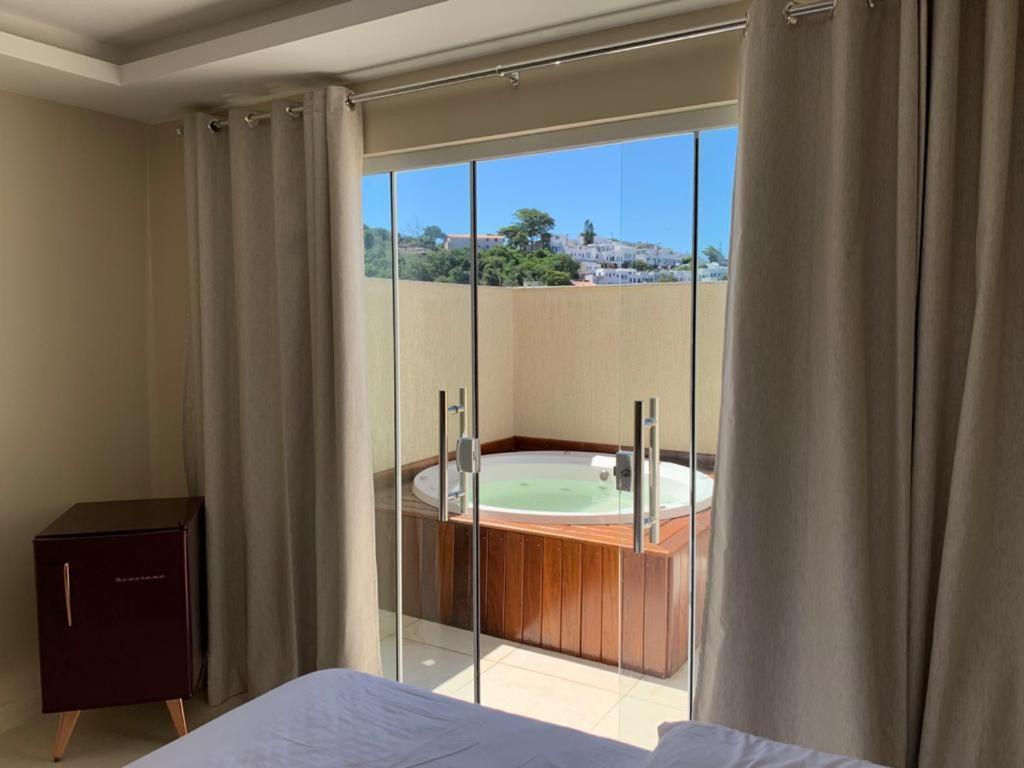 a bedroom with a large window with a bath tub at Pousada Arraial Tropical in Arraial do Cabo