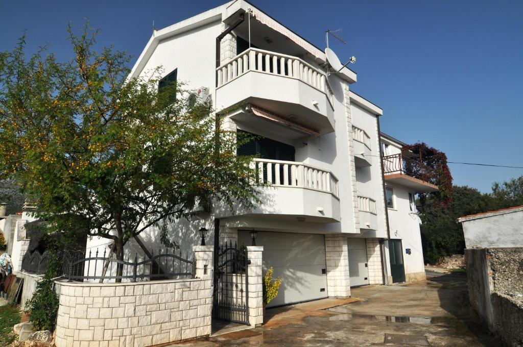 biały dom z balkonem i drzewem w obiekcie Apartmani Rokić w mieście Seget Vranjica