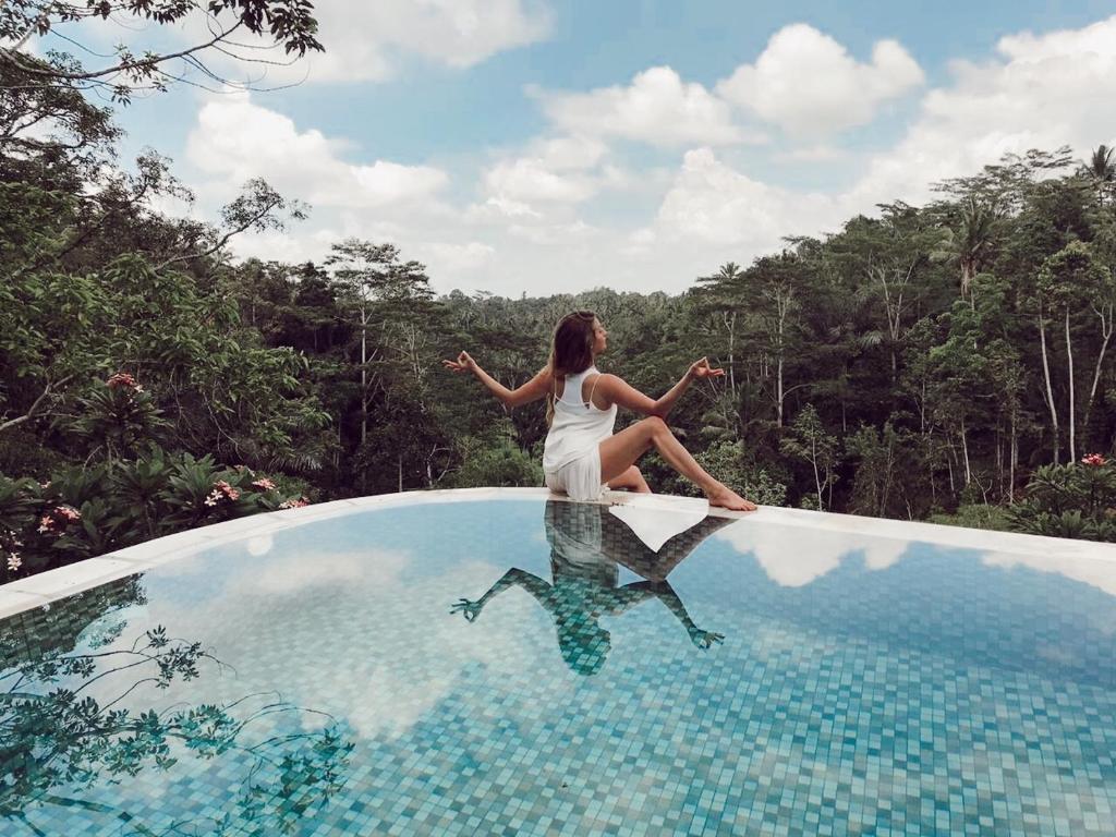 a woman sitting on the edge of a swimming pool at Yoga Maya Villa in Gianyar