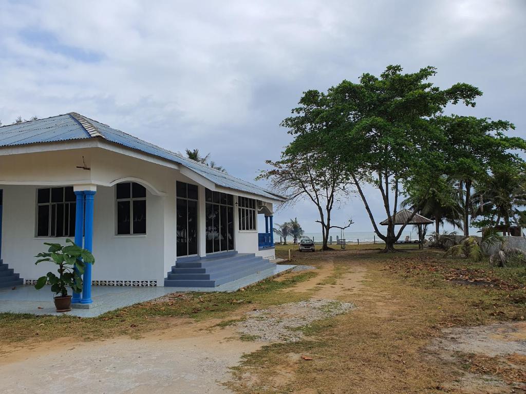 una casa blanca con adornos azules y un árbol en ALA Beach Lodge - Ketapang Homestay, en Kota Bharu