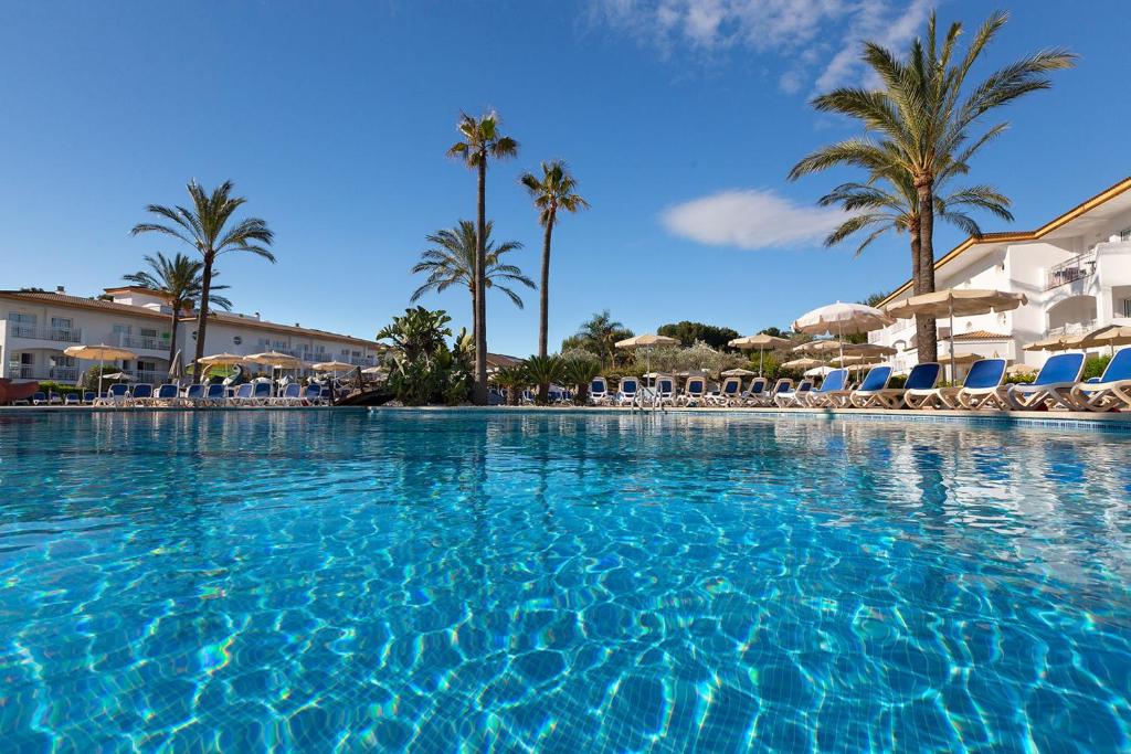 a large swimming pool with chairs and palm trees at Mar Hotels Playa Mar & Spa in Port de Pollensa