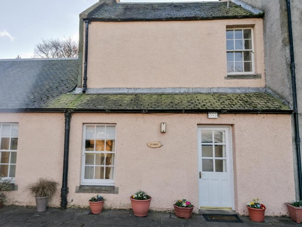 uma casa velha com uma porta branca e vasos de plantas em Turret Cottage em Prestonpans