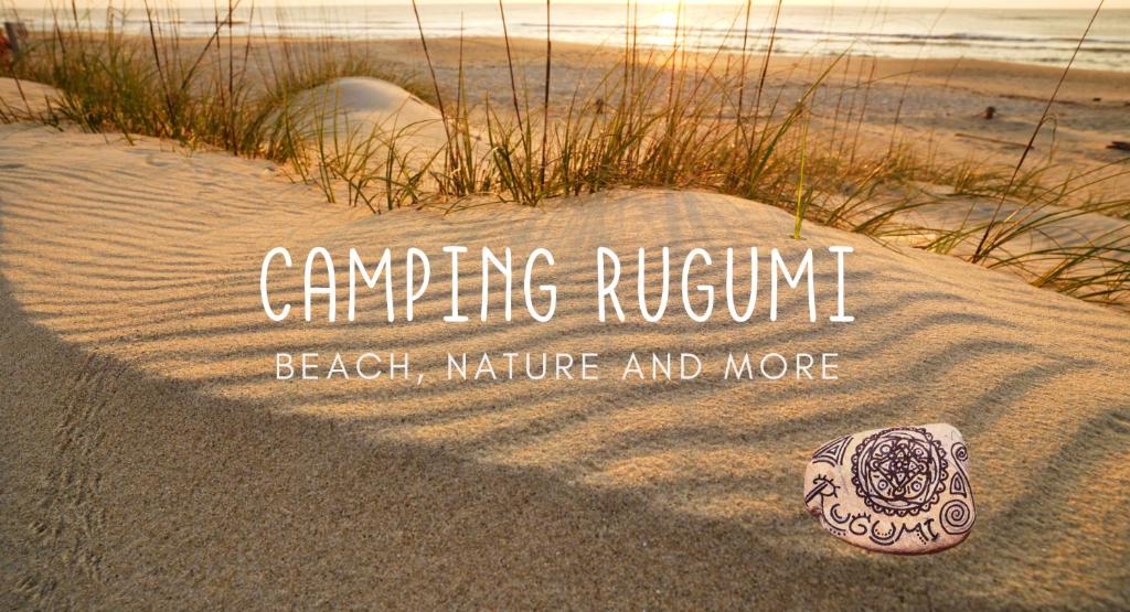 a sign on a beach with a rock in the sand at Camping Rugumi in Saraiķi